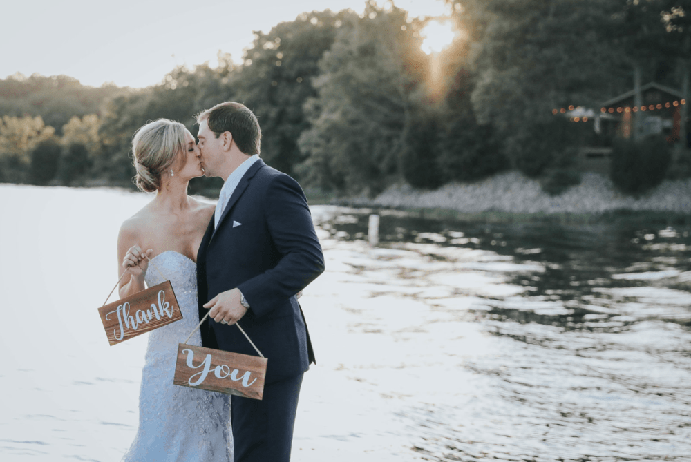 Bride and groom holding a thank you sign next to the lake on their wedding day